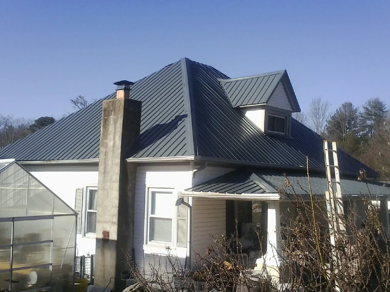 Dark blue standing seam metal roof on a white farmhouse with dormer — Slate & Tile Roof Repair by Roofing Brothers in Gratis