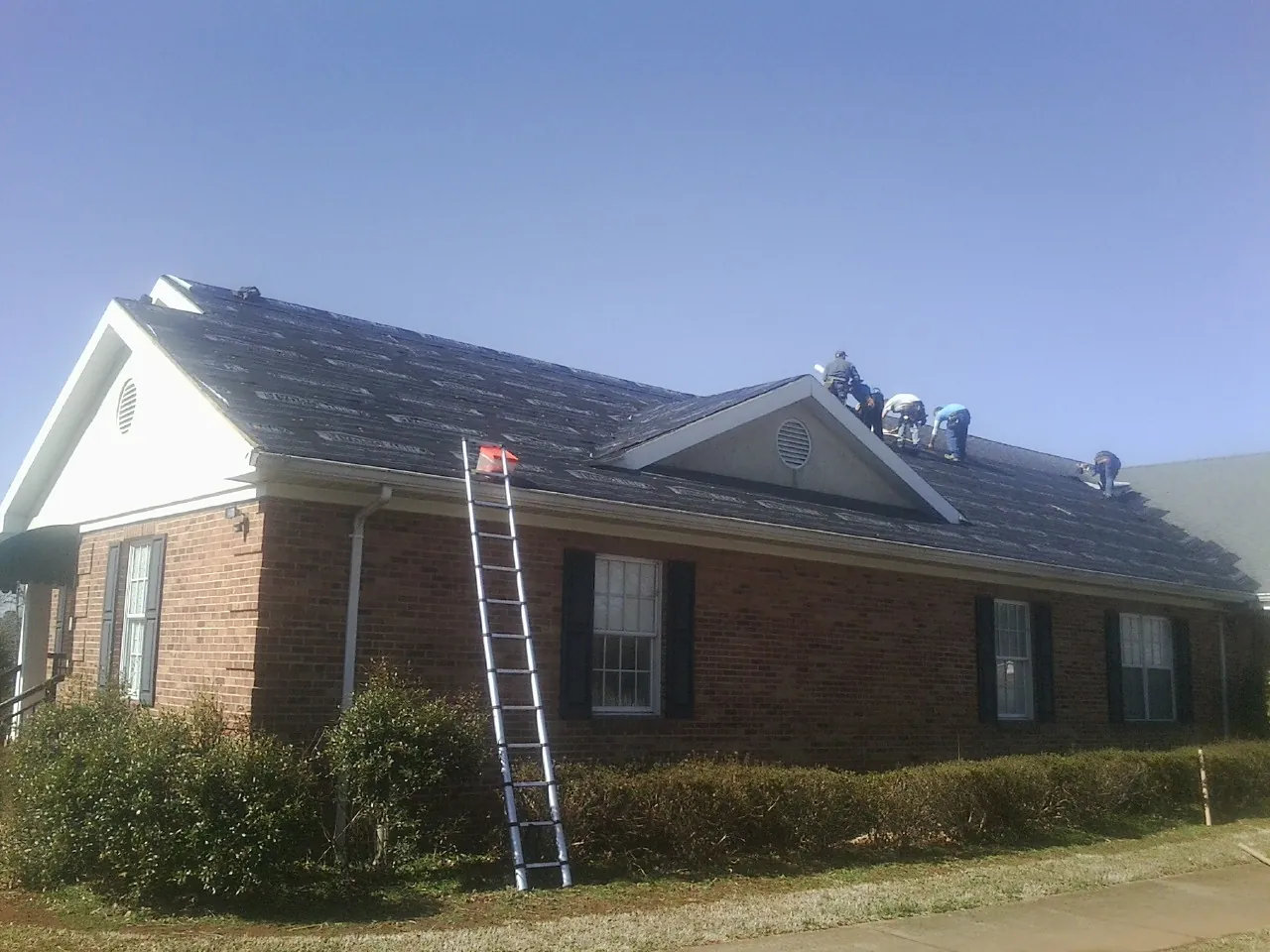 Crew tearing shingles off a brick ranch roof with a ladder set — Emergency Roof Repair work by our crew in Gratis