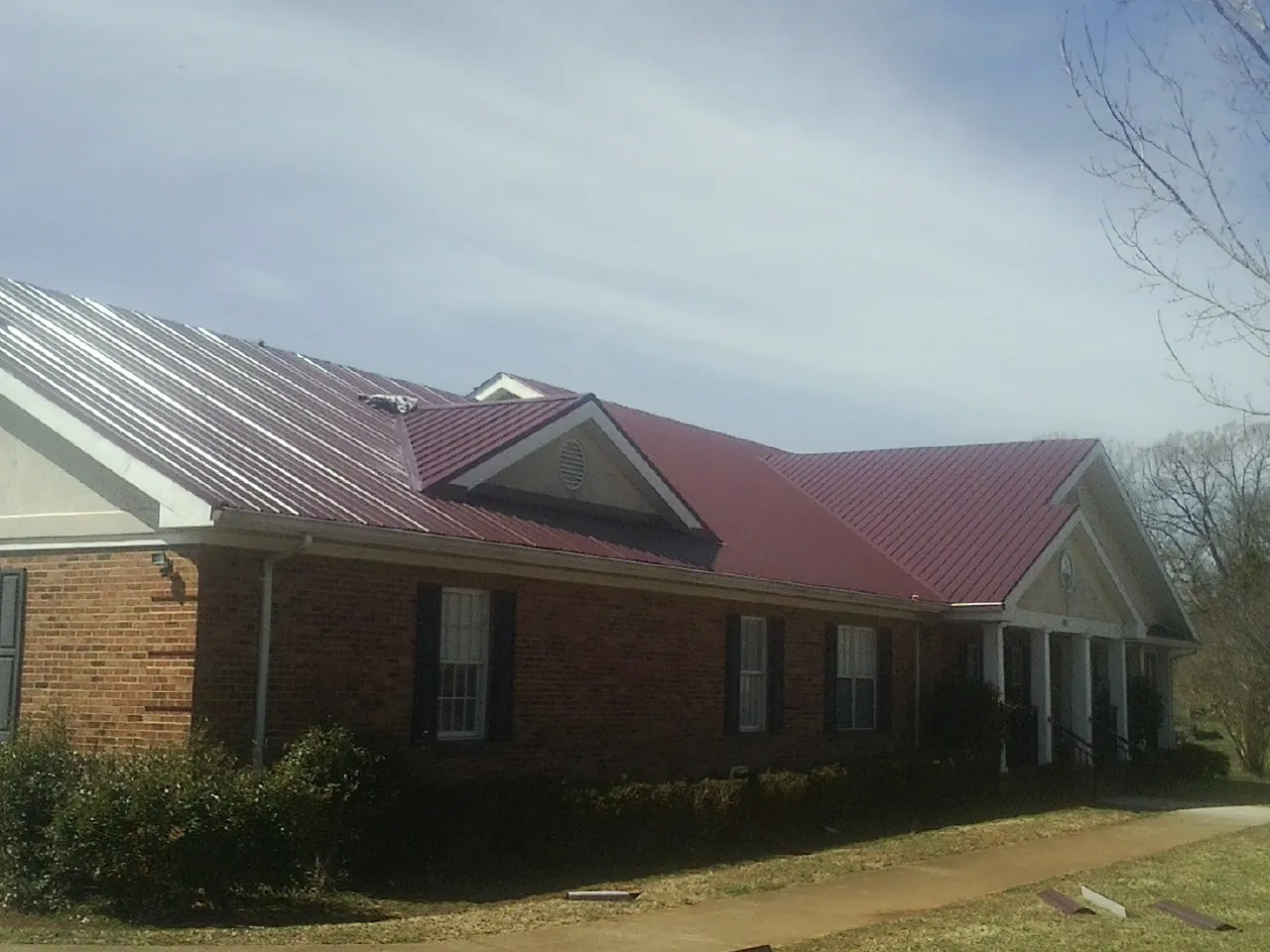 Red metal roof with gabled entries on a long brick building, from a Hail Damage Roof Repair job in Gratis
