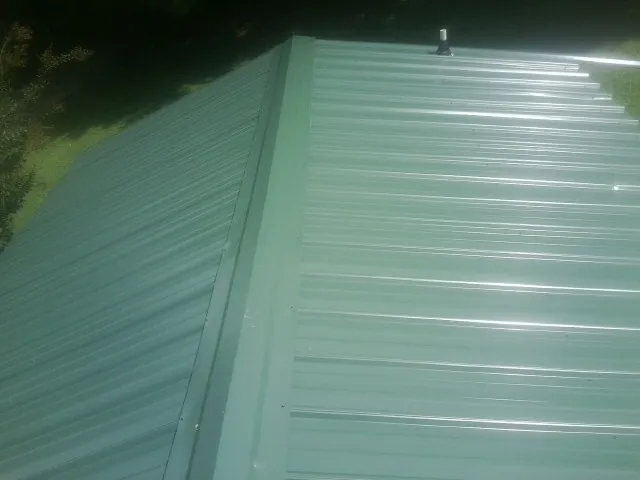 New green metal panels meeting at the ridge of a roof — Flat Roof Repair work by our crew in Gratis