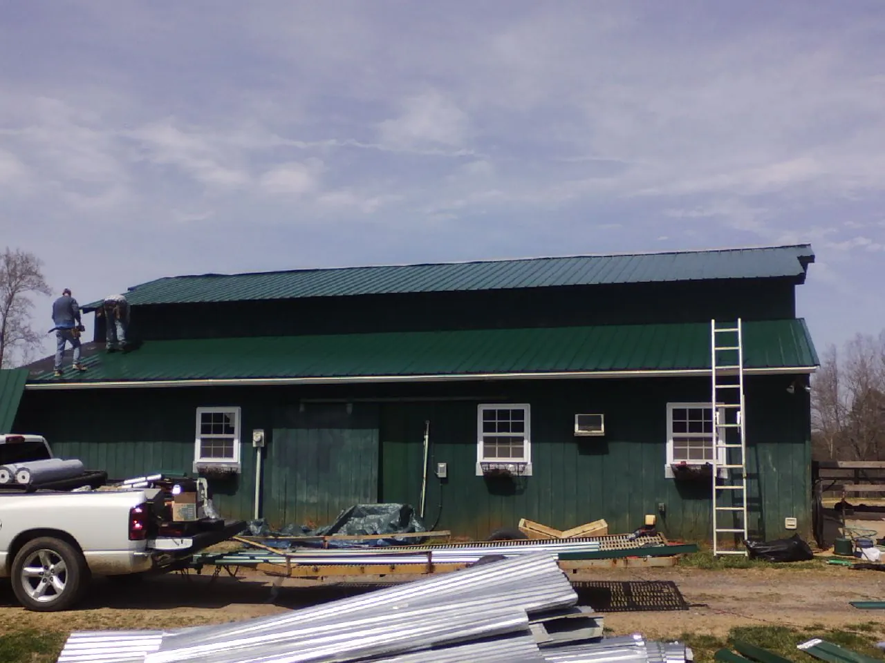 Crew installing green metal roofing on a large green barn in Gratis