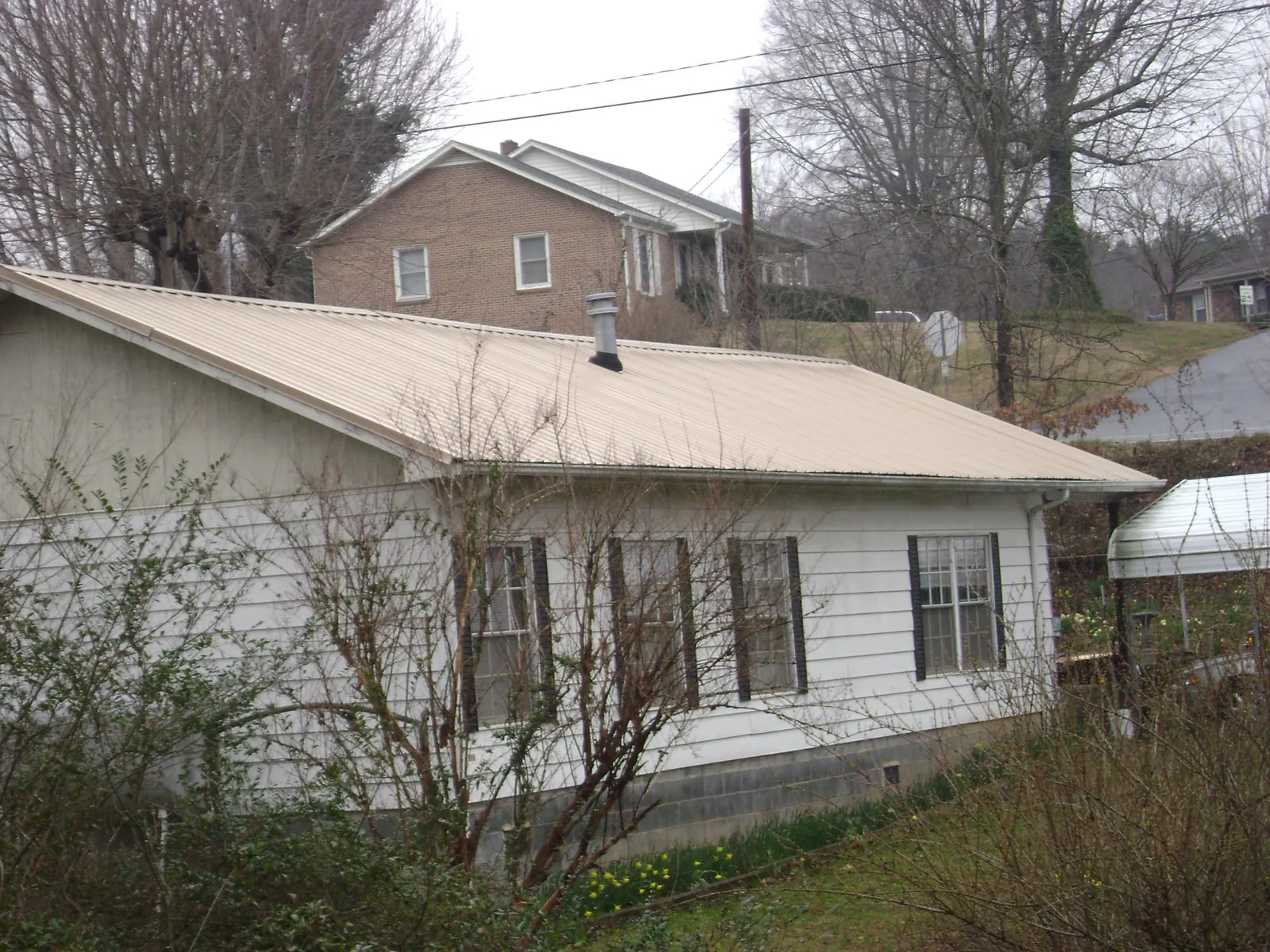 Tan metal roof on a white sided house set into a hillside — Commercial Roofing by Roofing Brothers in Gratis