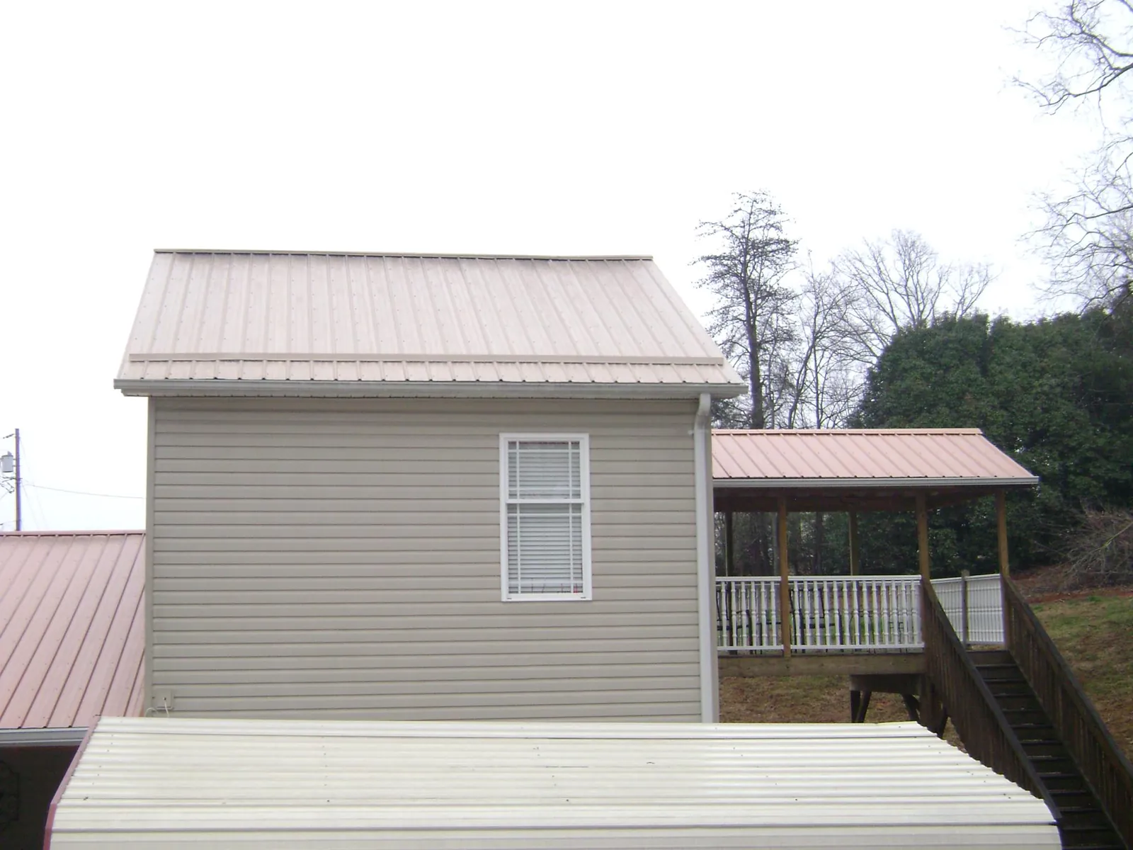Tan metal roofs on a two story addition and attached porch, from a Roof Replacement job in Gratis